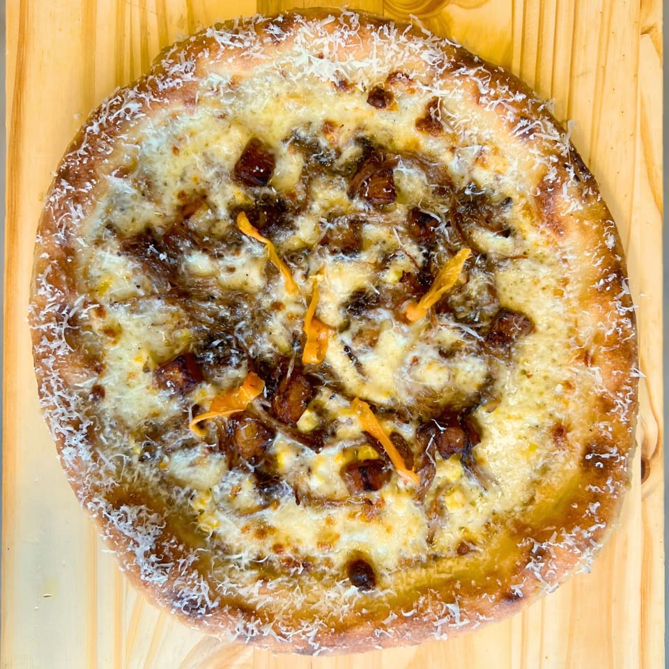 One World Pizza's white pizza with caramelized onions, cheese, and orange pepper strips on a wooden board.