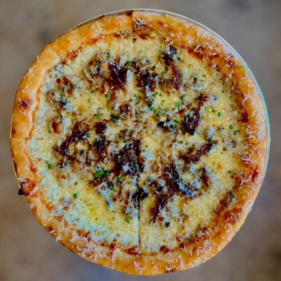 Overhead view of a One World Pizza with white cheese, dark toppings, and chives.