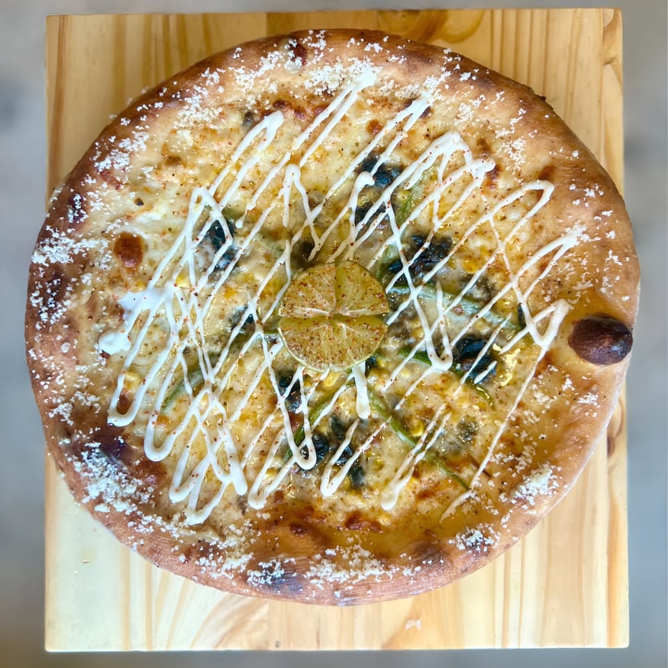 One World Pizza's white sauce pizza with green peppers, black olives, and a lime wedge.