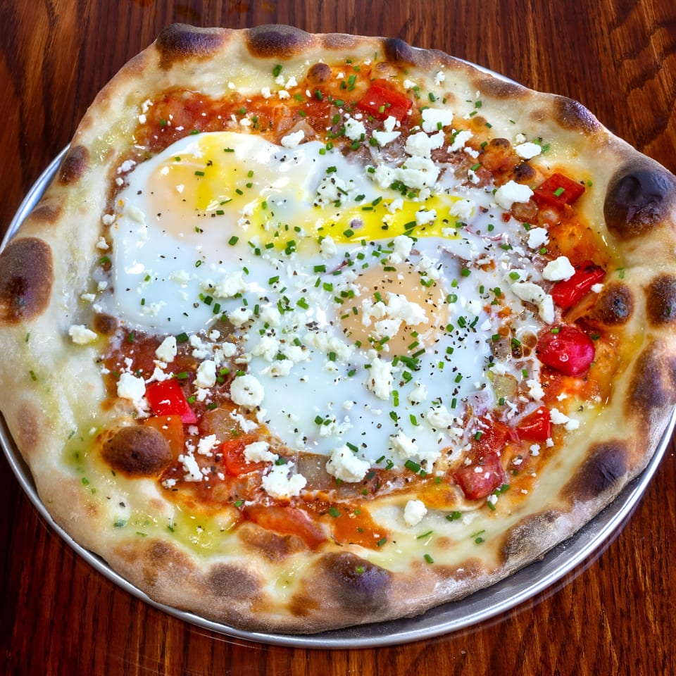 One World Pizza's breakfast pizza with eggs, feta, chives, and red peppers on a wooden table.