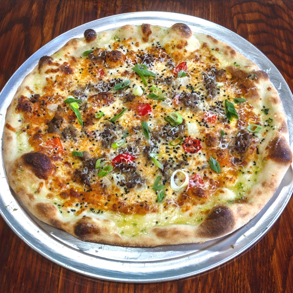 One World Pizza's specialty pizza with ground meat, red peppers, scallions, and black sesame seeds.